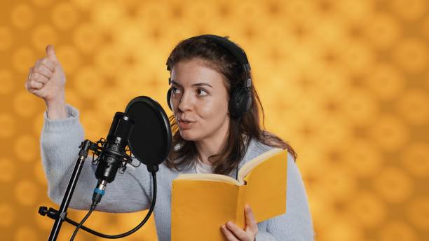 Voice actor looking to producer off camera to know when to start narrating book, producing audiobook. Narrator doing counting on fingers gesturing before starting digital recording of novel, camera A